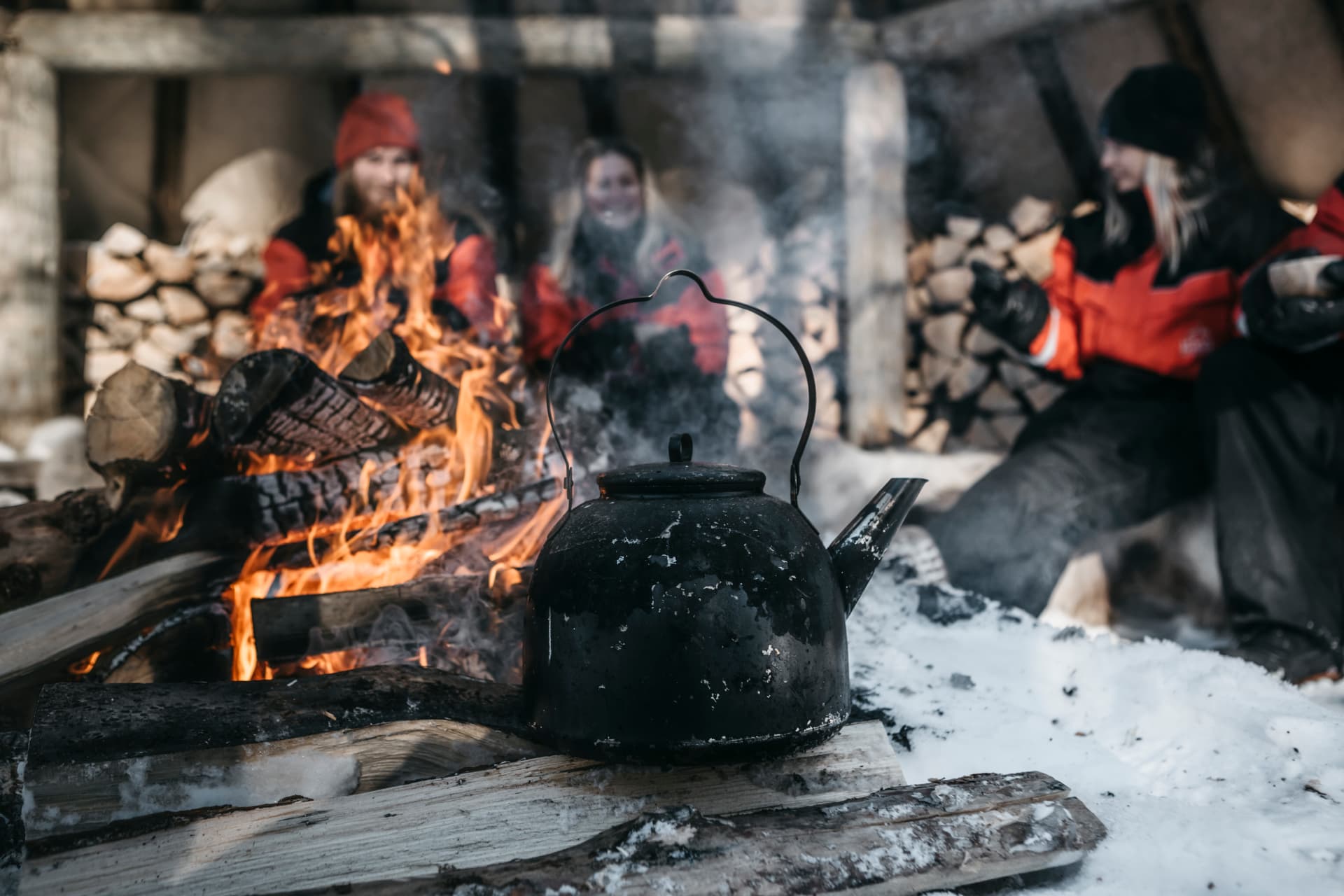 Blackened kettle over an open fire in a kota, guests warming beyond the flames