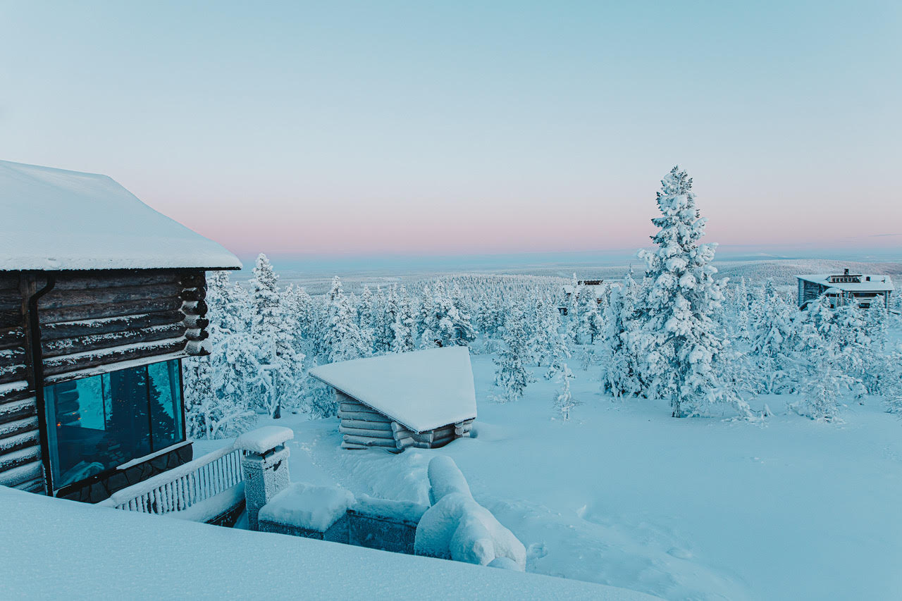 A villa terrace and sauna hut in deep snow above frozen forest as the sky turns pink