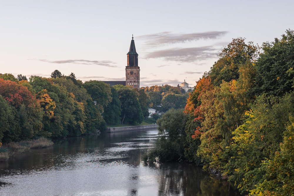 Turku Cathedral tower above the Aura river framed by autumn trees at dusk