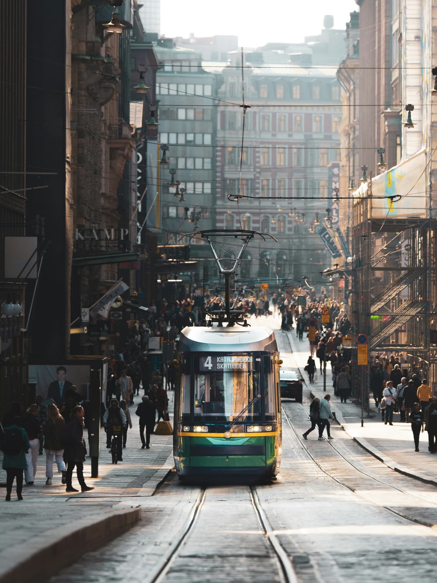A green tram running down a busy Helsinki shopping street in low golden light