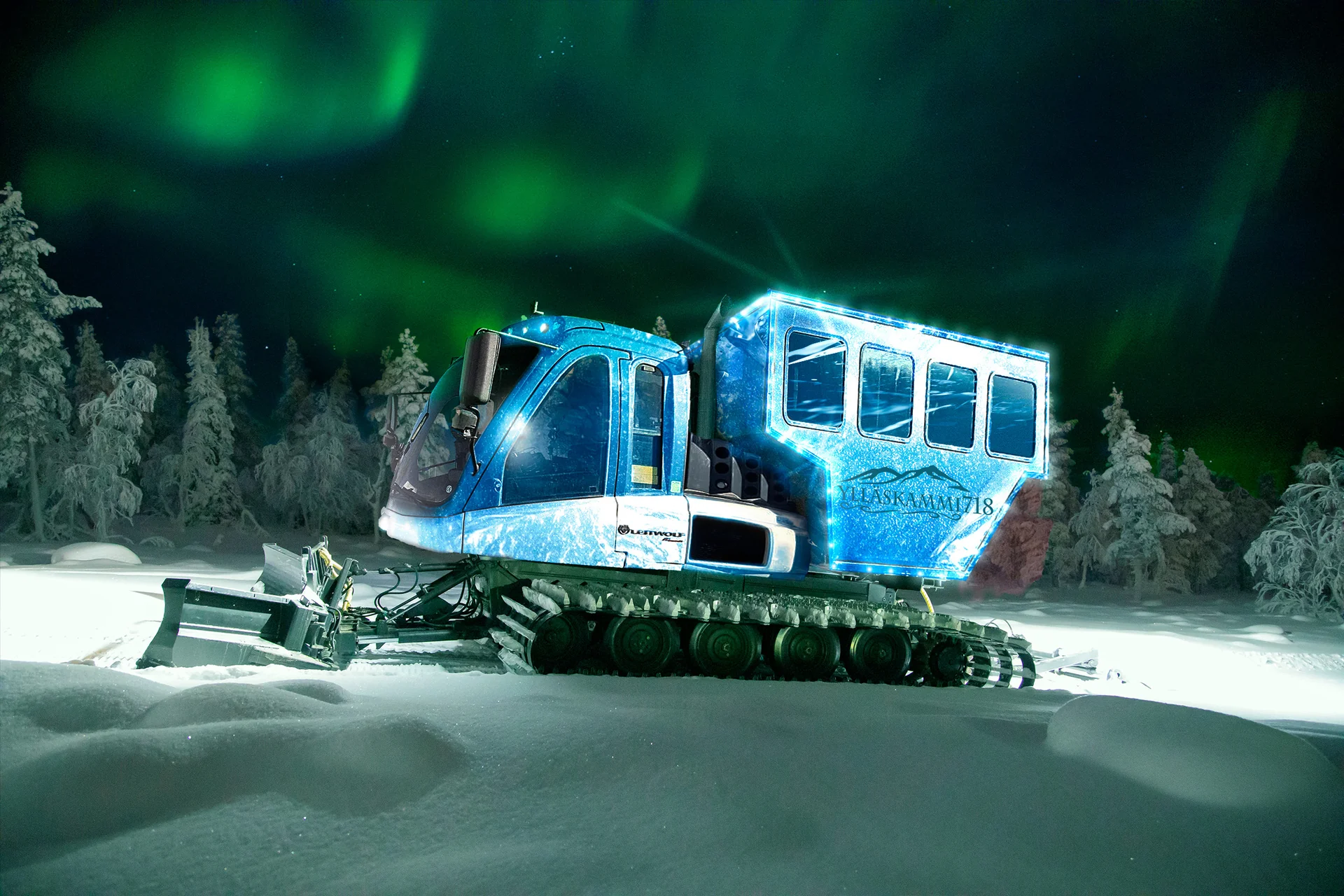 A lit snowcat cabin on the fells at Ylläs beneath a green aurora