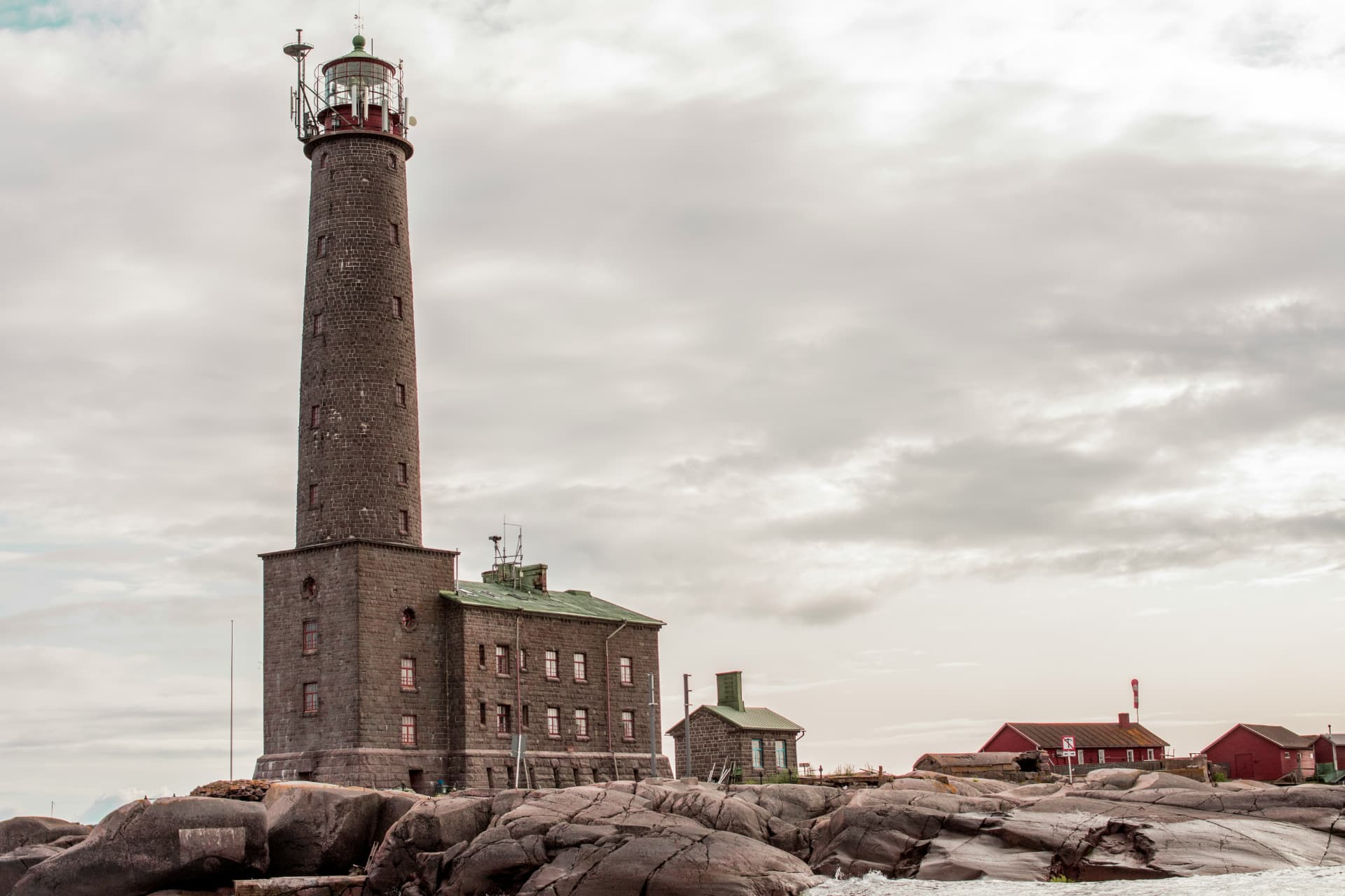 A tall stone lighthouse and keeper's house on wave-washed rocks in the outer archipelago